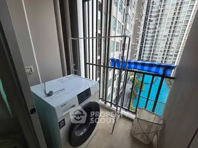 Compact balcony with washing machine overlooking pool and modern high-rise buildings.
