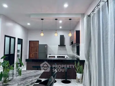 Modern kitchen with sleek design, featuring a marble dining table, pendant lights, and stainless steel appliances.