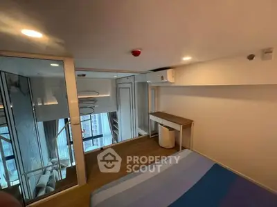 Modern bedroom with mirrored closet and wooden desk, featuring city view from window.