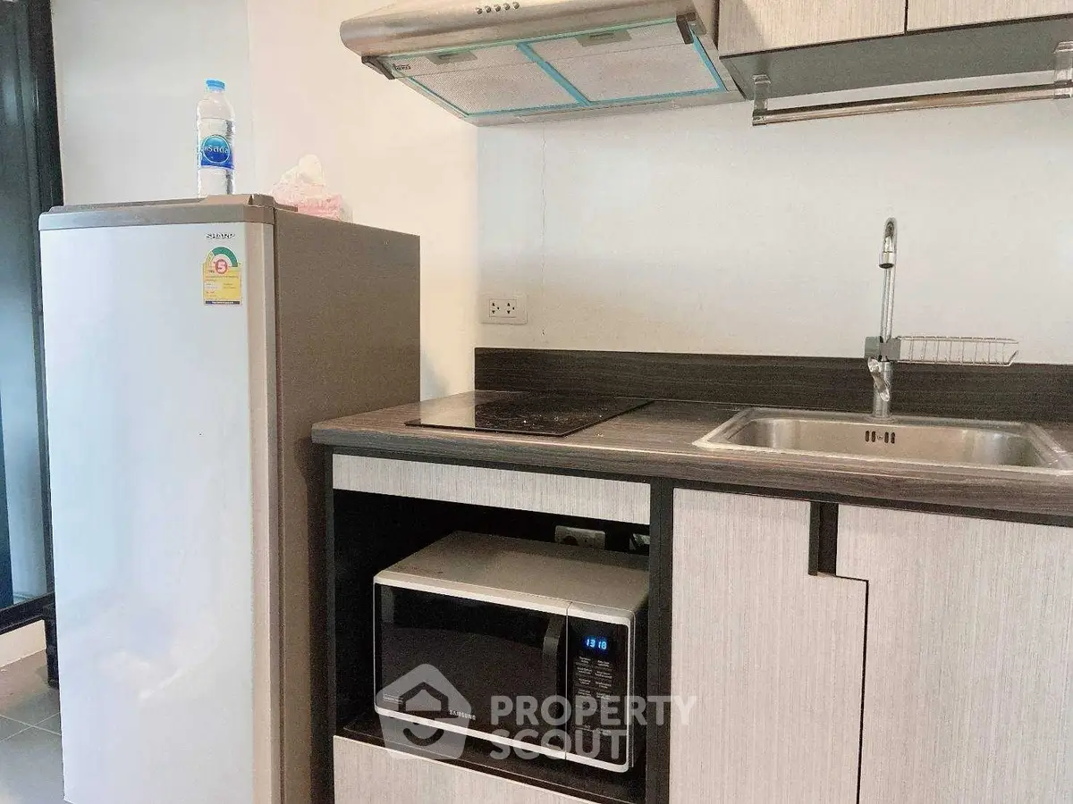 Modern kitchen with sleek appliances including fridge, microwave, and stovetop in compact layout.