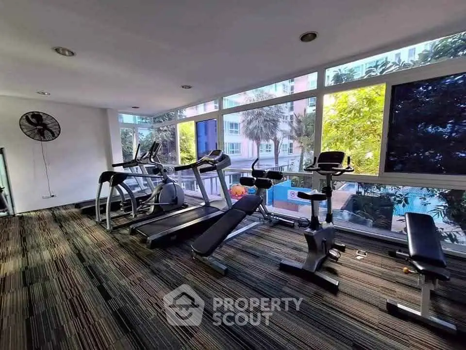 Modern gym with cardio equipment and large windows offering a pool view.