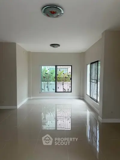 Spacious living room with large windows and glossy tiled floors, offering a bright and airy atmosphere.