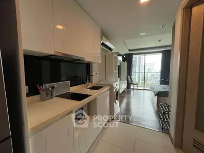 Modern studio apartment with sleek kitchen and city view, featuring built-in appliances and stylish decor.