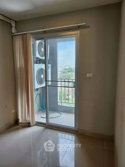 Bright room with sliding glass door leading to a small balcony with city view and air conditioning unit.