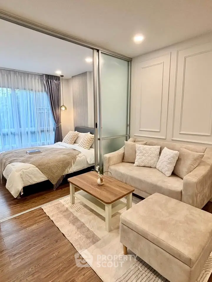 Modern studio apartment with cozy living area and elegant bedroom separated by glass partition.