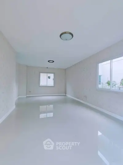 Spacious empty room with glossy white flooring and large windows for natural light.