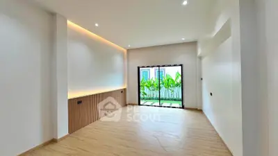 Spacious modern living room with large window and garden view, featuring elegant lighting and wooden flooring.