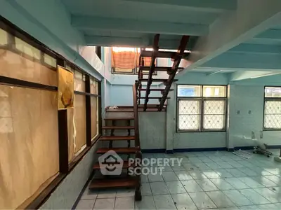 Spacious interior with wooden staircase and large windows, ideal for renovation.