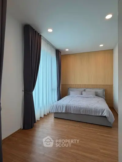 Modern bedroom with elegant curtains and wooden flooring, featuring a cozy bed and stylish wall paneling.