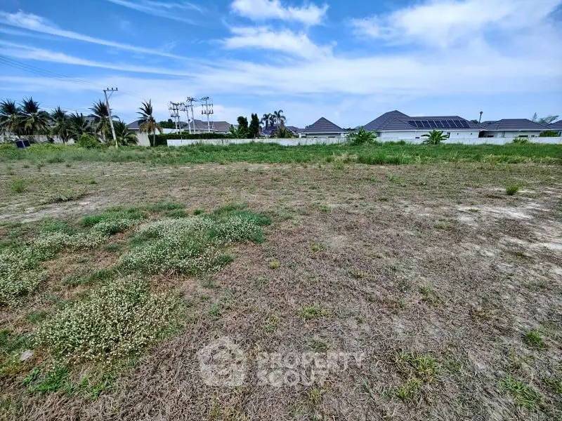 Expansive vacant land with potential for development, surrounded by greenery and clear blue skies.