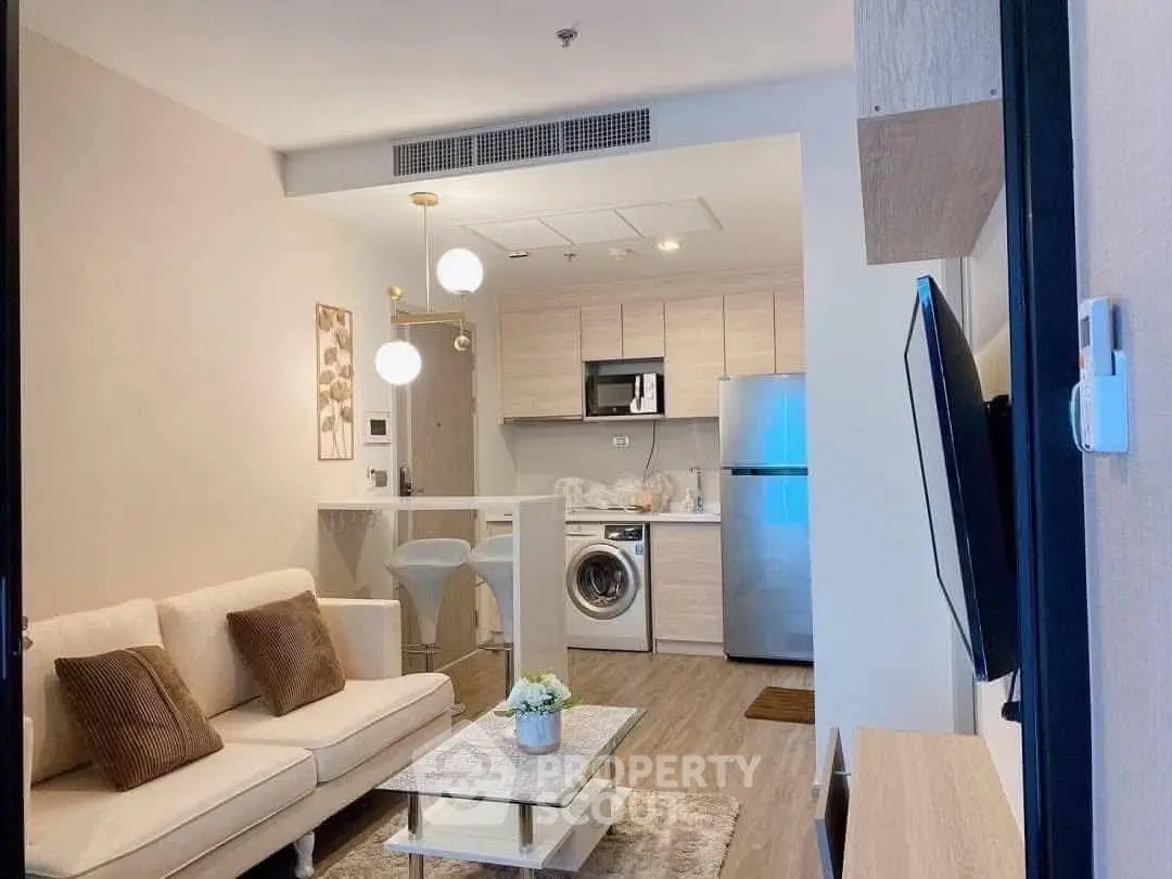 Modern living room with open kitchen, featuring cozy sofa and stainless steel appliances.