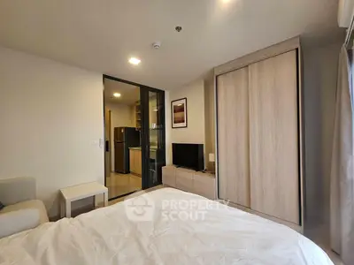 Modern bedroom with sliding glass door to kitchen, featuring sleek furniture and neutral tones.