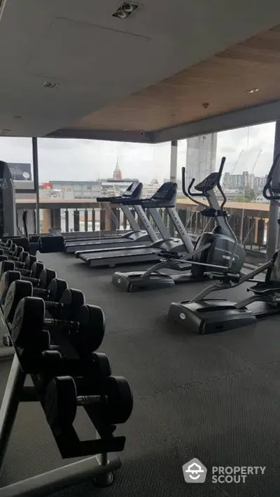 Modern gym with city view featuring treadmills and weights in a high-rise building.