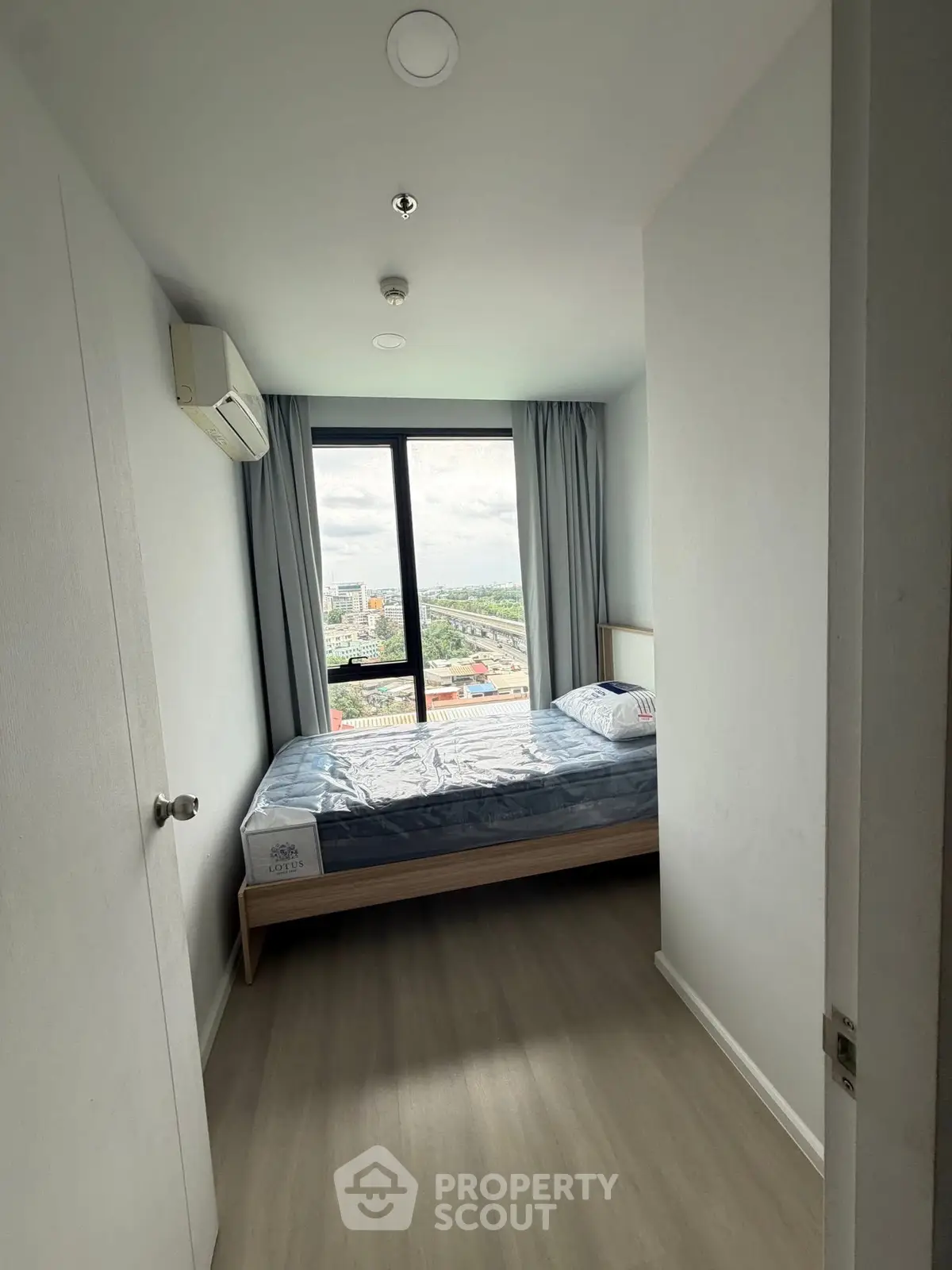 Modern bedroom with large window offering stunning city view, featuring minimalist design and air conditioning.