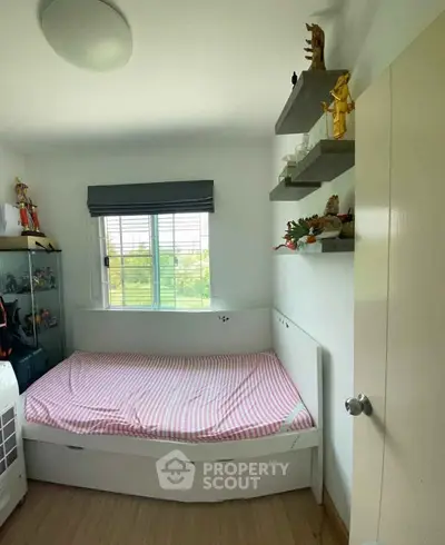 Cozy bedroom with single bed, window view, and decorative shelves in a modern apartment.