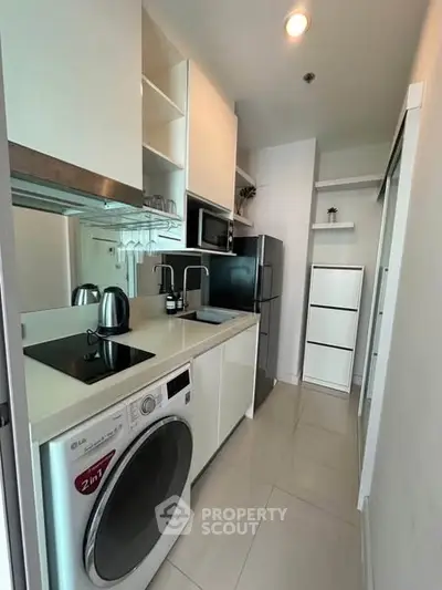 Modern compact kitchen with sleek appliances and washing machine in a stylish apartment.