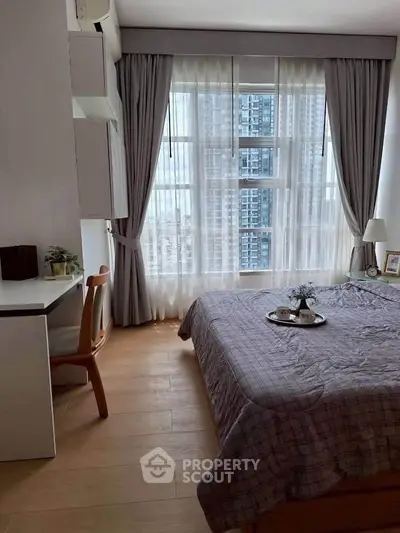 Cozy bedroom with large window offering city view, featuring a study desk and elegant decor.