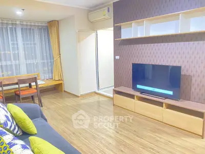 Modern living room with stylish decor and large TV, featuring wooden flooring and ample natural light.