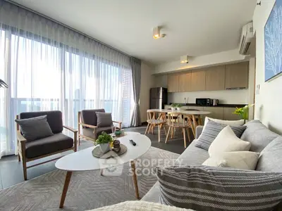 Modern living room with open kitchen, stylish furniture, and large windows for natural light.