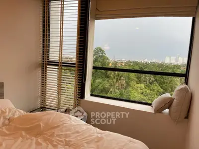 Cozy bedroom with large window offering stunning city and greenery views.