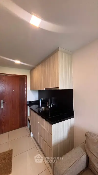 Modern compact kitchen with sleek black countertops and wooden cabinetry in a cozy apartment setting.