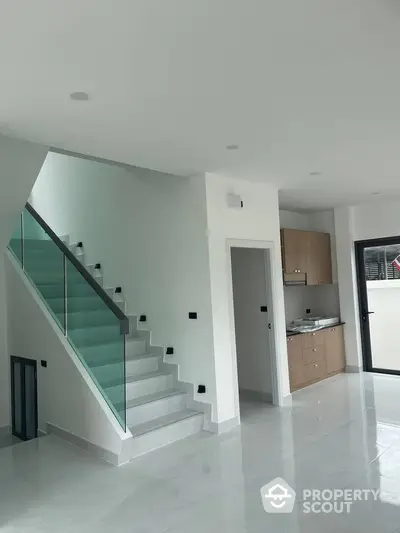 Modern minimalist interior with sleek staircase and compact kitchen area.