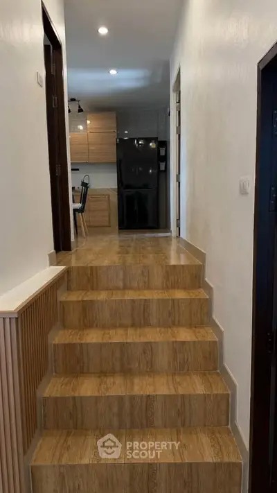 Modern hallway leading to a stylish kitchen with wooden flooring and sleek black appliances.