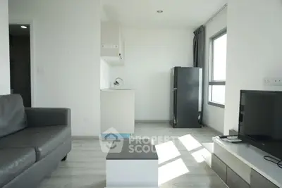 Modern living room with sleek furniture and natural light, featuring a compact kitchen and large window.