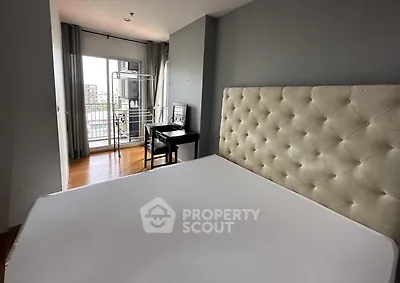 Modern bedroom with plush headboard and balcony access in urban apartment.