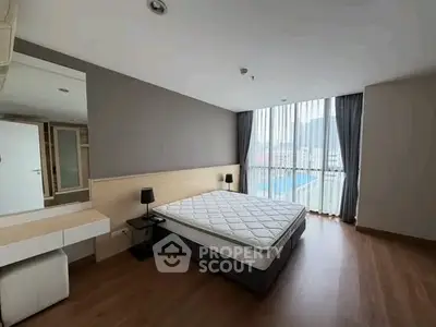Spacious bedroom with large window and modern furnishings in a stylish apartment.