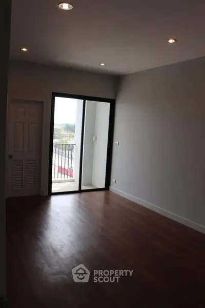 Spacious empty room with wooden flooring and balcony access in modern apartment.