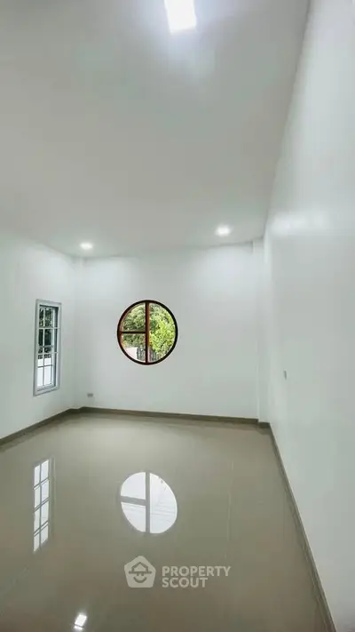 Spacious minimalist room with unique round window and glossy tiled floor, perfect for modern living.