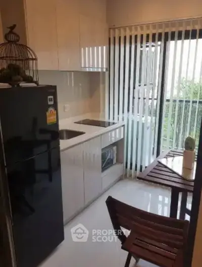 Modern kitchen with sleek cabinetry and balcony view, featuring a compact dining area and natural light.