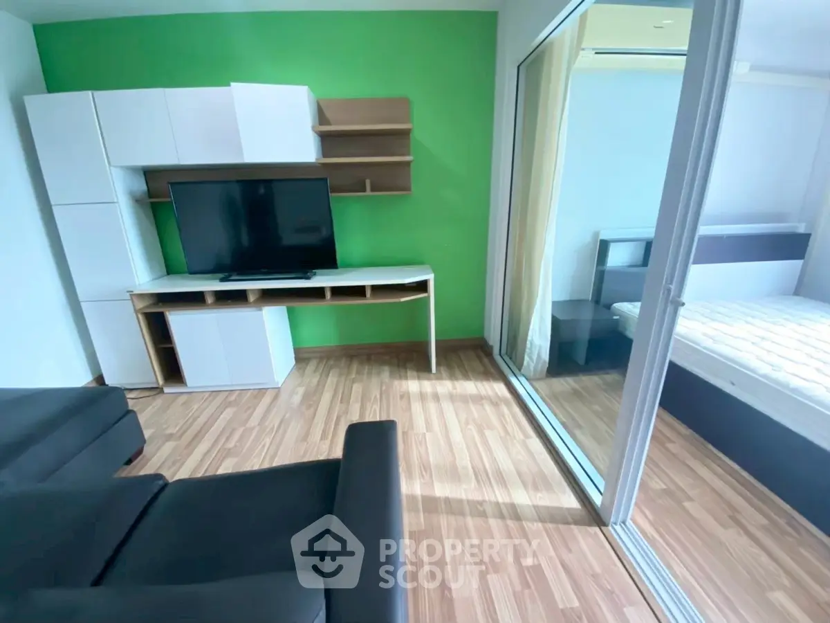Modern living room with sleek furniture and green accent wall adjacent to a cozy bedroom.