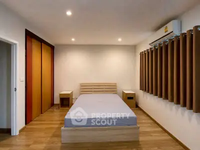 Modern bedroom with minimalist design, featuring wooden flooring and air conditioning.