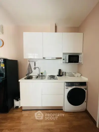 Compact kitchen with modern appliances and washing machine in cozy apartment.