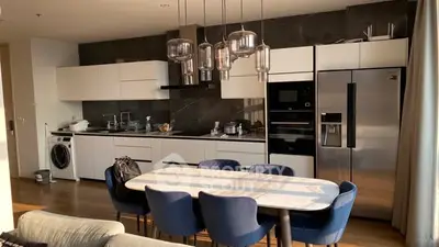 Modern kitchen with sleek appliances and dining area, featuring a washing machine and stylish lighting.
