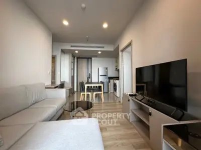 Modern living room with open kitchen, featuring sleek furniture and wooden flooring.