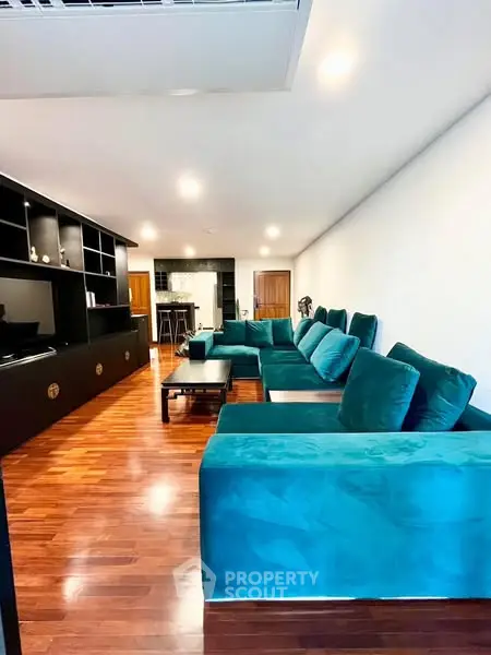Spacious living room with teal sectional sofa and wooden flooring, perfect for modern living.