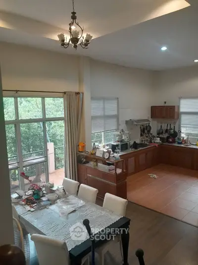 Spacious kitchen with dining area and large windows overlooking greenery, featuring modern appliances and elegant decor.