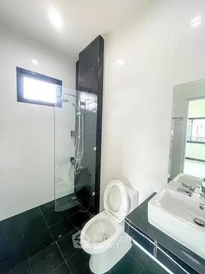 Modern bathroom with sleek black and white tiles, glass shower, and contemporary fixtures.