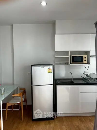 Modern kitchen with sleek white cabinets, stainless steel fridge, and built-in microwave in a cozy apartment.