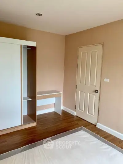 Spacious bedroom with wooden flooring and built-in wardrobe in modern apartment.