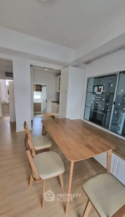 Modern dining area with wooden table and chairs, adjacent to a sleek kitchen with ample natural light.