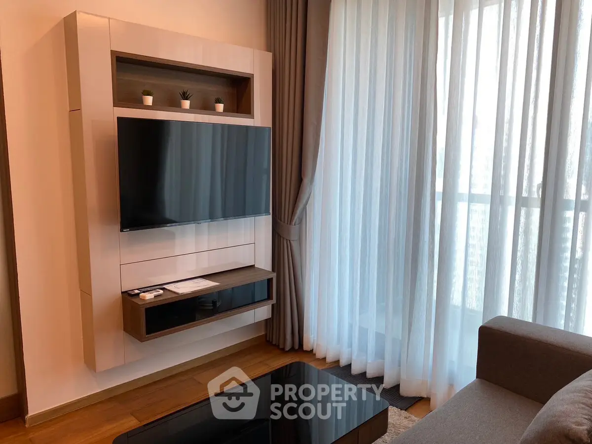 Modern living room with wall-mounted TV and large window with sheer curtains.