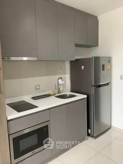 Modern kitchen with sleek cabinetry, stainless steel fridge, and built-in microwave in a compact layout.