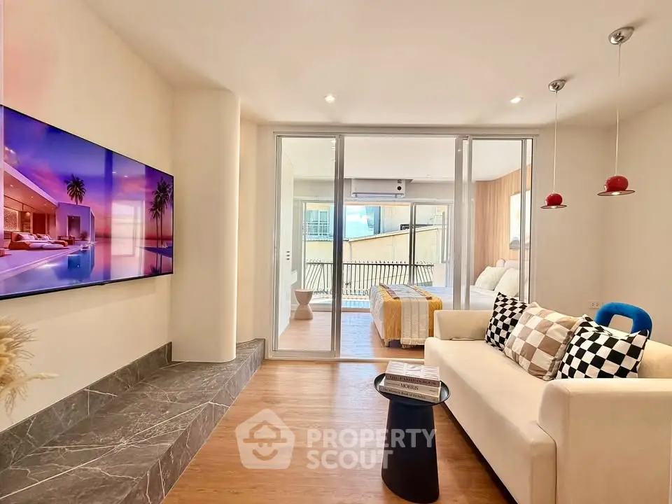 Modern living room with stylish decor and balcony view, featuring a large wall-mounted TV and cozy seating area.