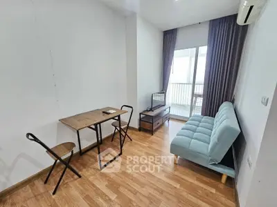 Cozy living room with wooden flooring, compact furniture, and balcony access.