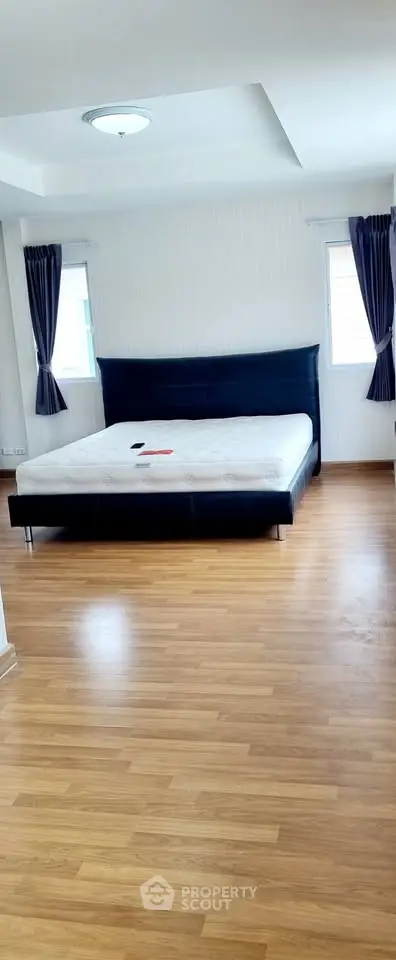 Spacious bedroom with modern bed and wooden flooring, ample natural light from windows.