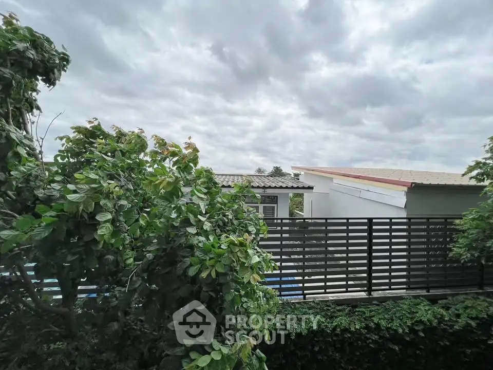 Charming suburban home with lush greenery and modern fencing under a cloudy sky.